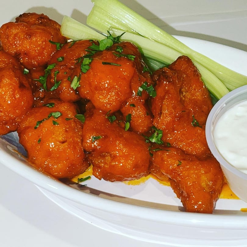 Buffalo chicken wings with celery sticks and a side of ranch dressing on a white plate.