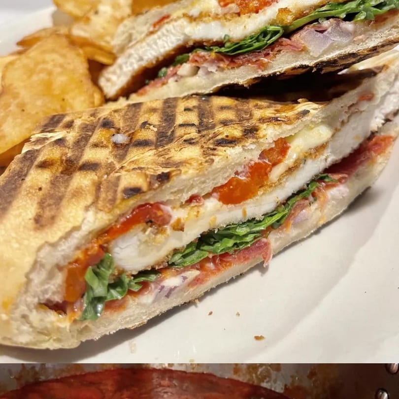 Grilled Italian panini with chicken, red peppers, prosciutto, and arugula, served with potato chips.